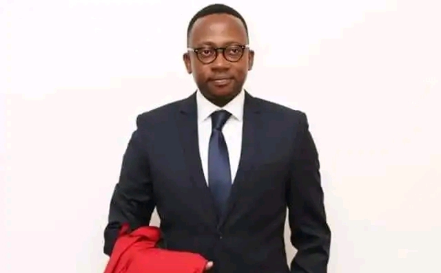Homme en costume sombre et cravate tenant une veste rouge devant un mur blanc