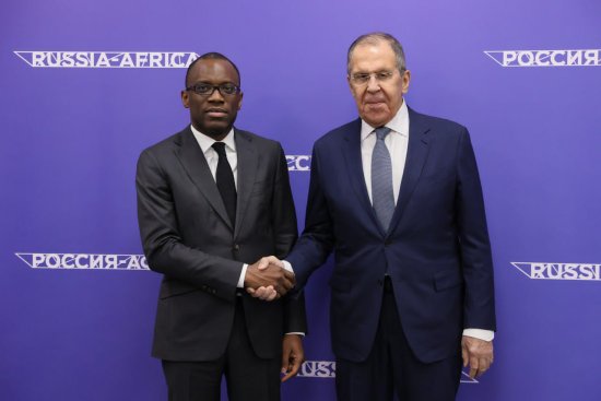 Deux hommes en costume cravate se serrent la main devant un fond bleu avec inscriptions « RUSSIA-AFRICA » et écriture en cyrillique