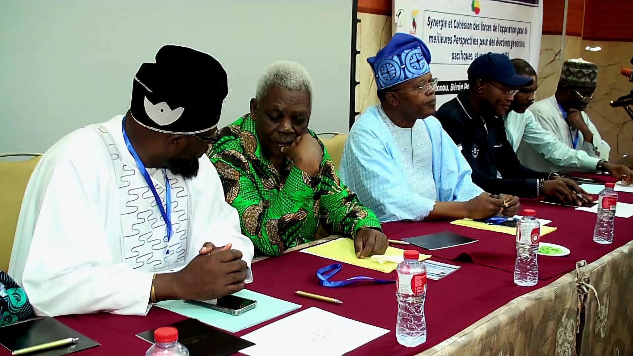 Un groupe d’hommes assis à une table recouverte d’une nappe rouge discutant lors d’une réunion en intérieur