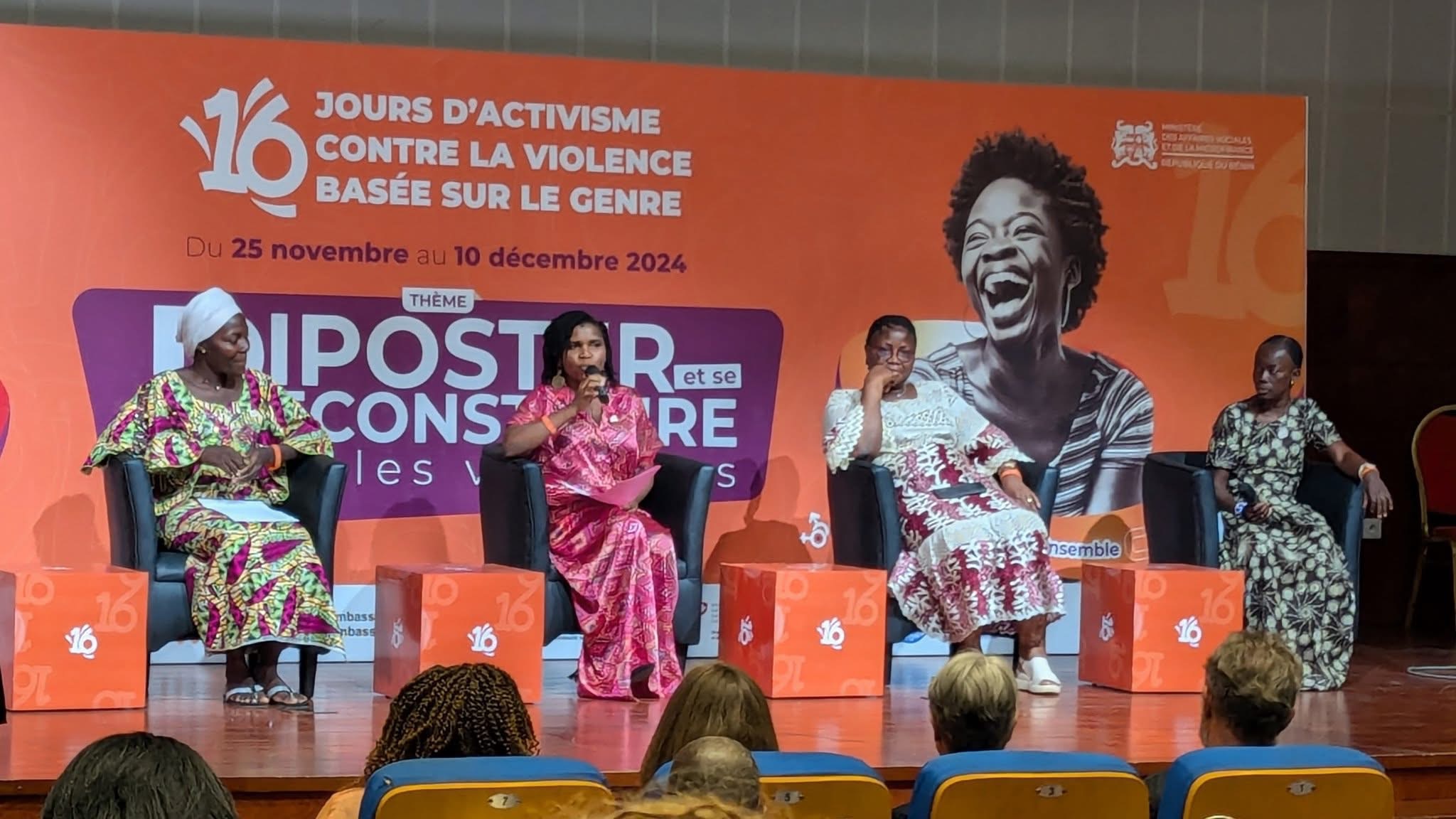 Quatre femmes assises sur scène participent à une table ronde devant un grand panneau orange sur les violences basées sur le genre
