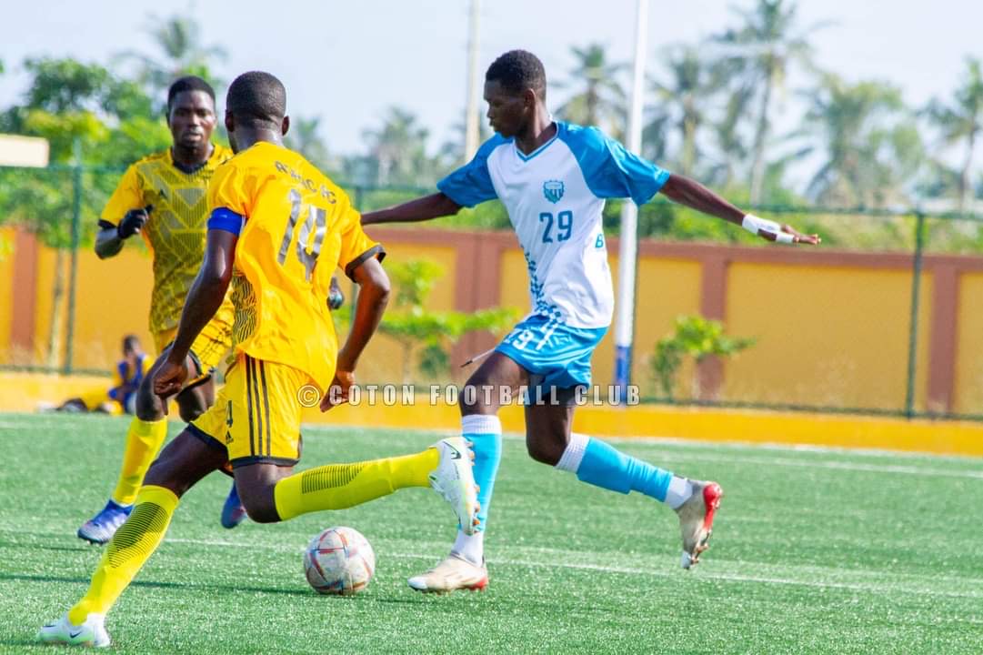 Deux joueurs en maillots jaune et un joueur en maillot blanc et bleu disputent un ballon sur un terrain de football en gazon synthétique