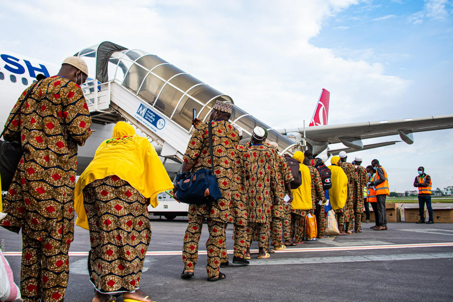 Des passagers habillés en tenues traditionnelles font la queue pour embarquer dans un avion au sol sur un aéroport