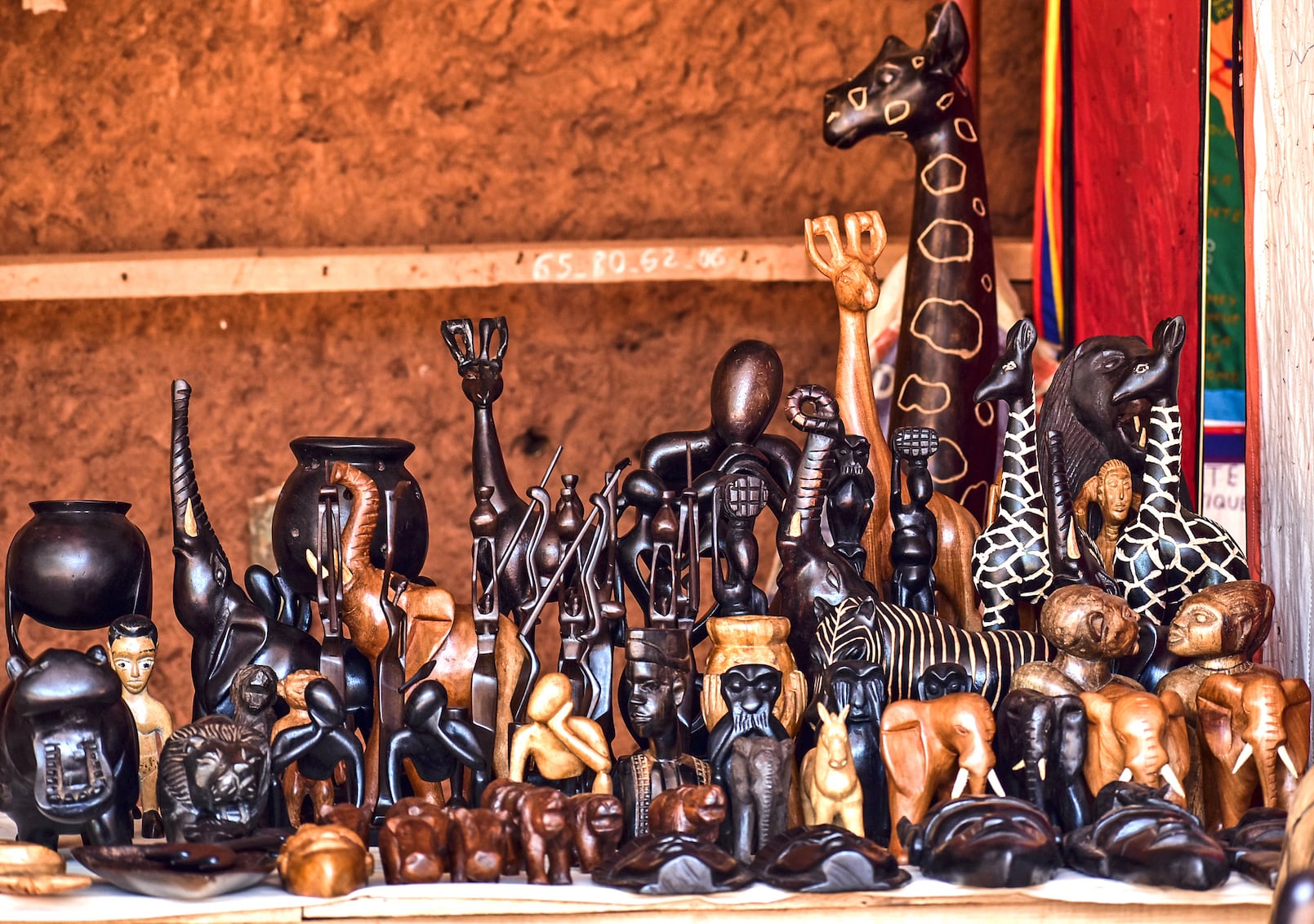 Personnages, animaux et objets sculptés en bois disposés en rangées sur une table devant un mur en terre battue