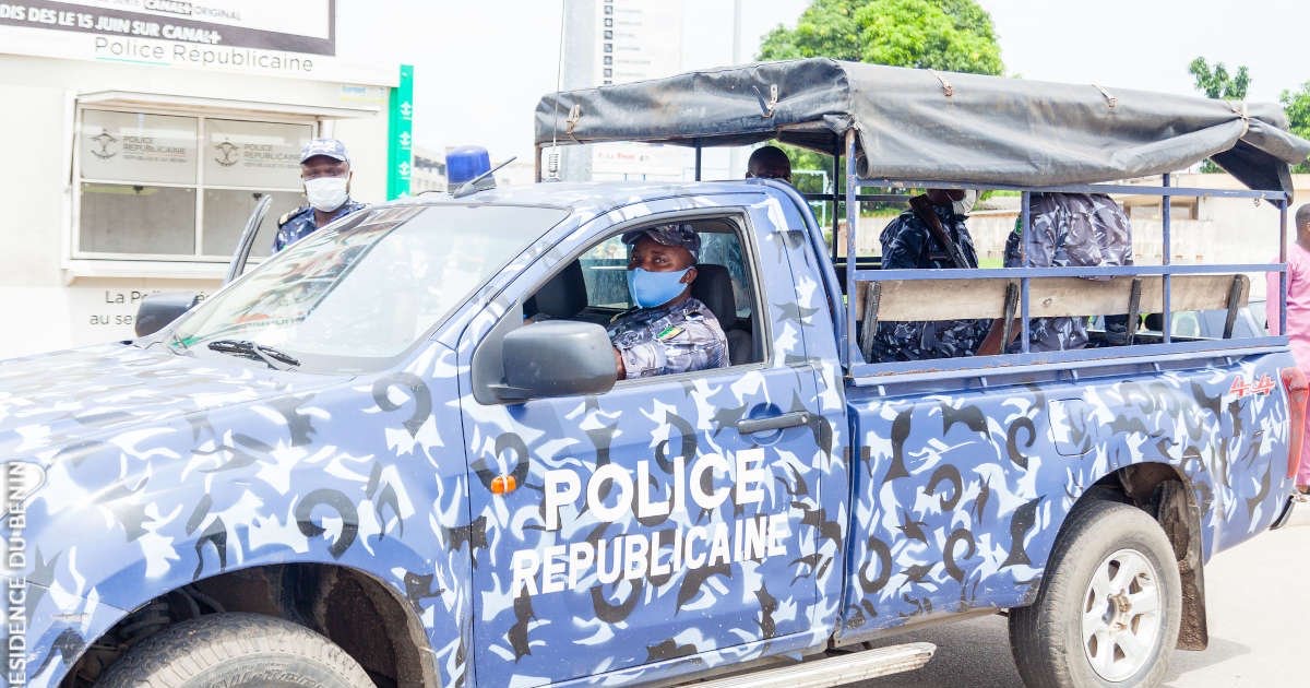 Véhicule de police bleue camouflée avec deux agents portant un masque dans et autour du véhicule stationné près d’un bâtiment