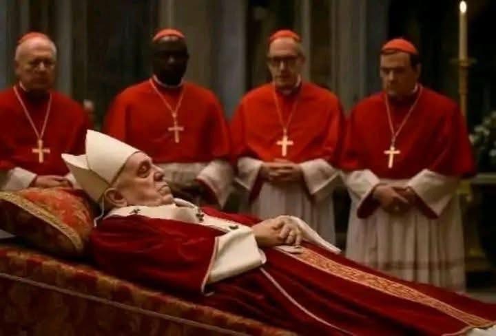 Un homme vêtu d’habits religieux blancs et rouges est allongé sur un lit, entouré de quatre hommes en robe rouge avec colliers croix.