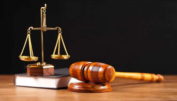 Balance de justice dorée posée sur un livre à côté d’un marteau en bois sur une table en bois