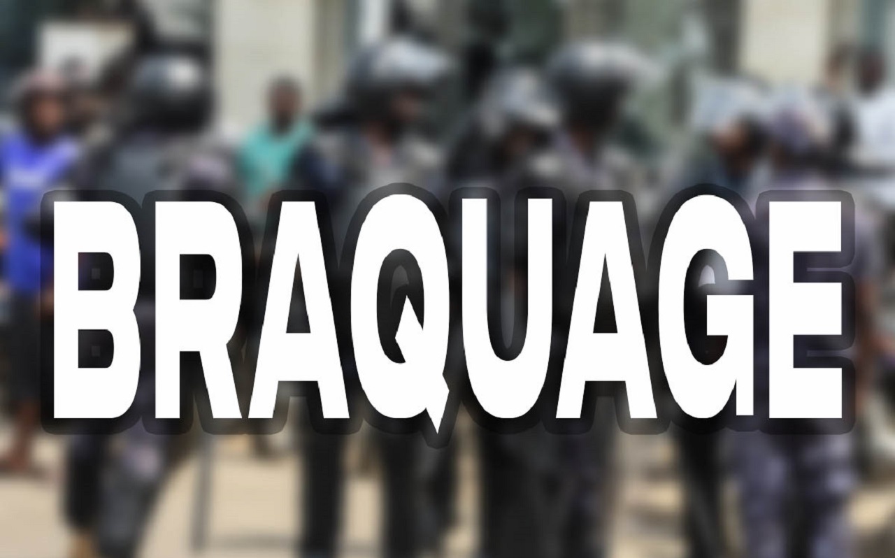 Des hommes en tenue de maintien de l’ordre avec des casques, vus derrière un texte en gros caractères BRAQUAGE