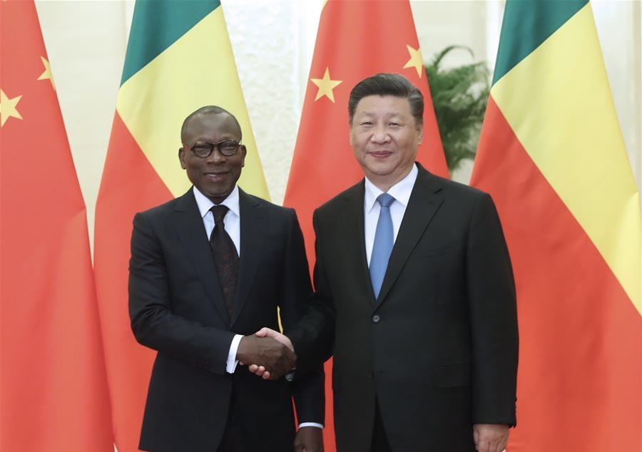 Deux hommes en costume noir se serrent la main devant trois drapeaux chinois et deux drapeaux jaunes, verts et rouges