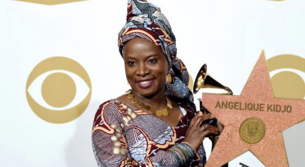 Une femme souriante en tenue traditionnelle colorée tient une étoile sur le Hollywood Walk of Fame avec un trophée Grammy à la main