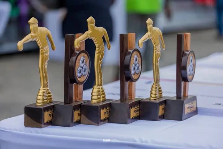 Cinq trophées dorés représentant un joueur de pétanque alignés sur une table blanche
