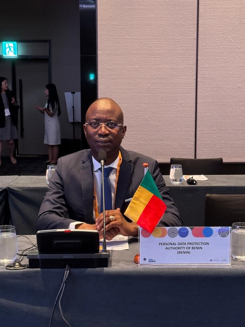 Homme assis à une table avec microphone et petit drapeau tricolore jaune, rouge, vert devant un panneau indiquant une autorité de protection des données personn