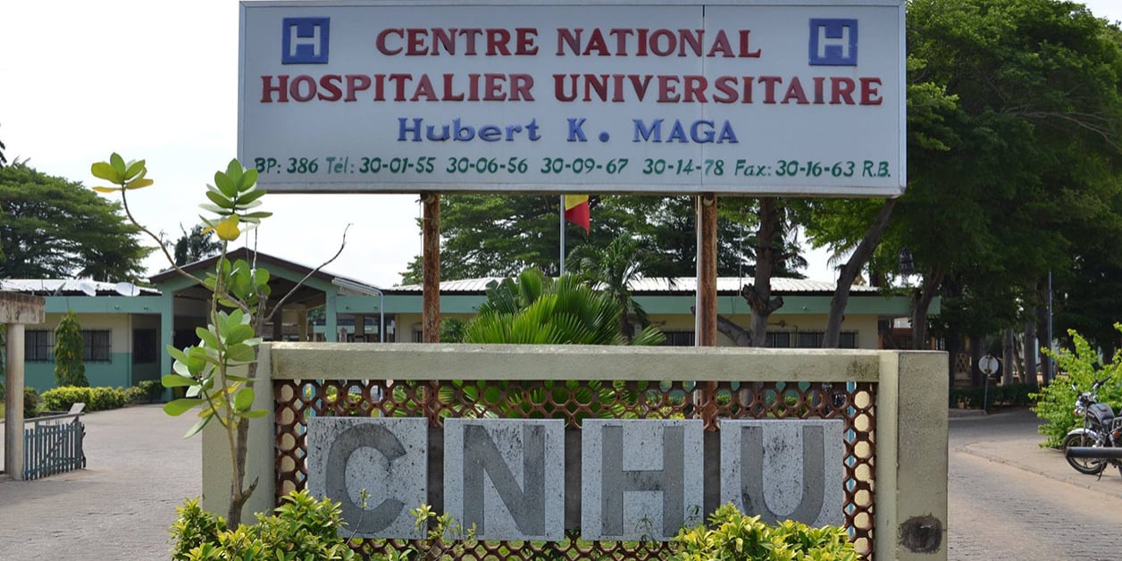 Entrée principale d'un centre hospitalier universitaire avec un grand panneau portant son nom et plusieurs numéros de téléphone visibles