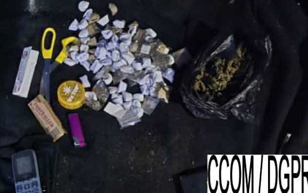 Plusieurs sachets transparents contenant une substance verte, un briquet violet, un cutter jaune, un grinder jaune et un téléphone posés sur un tissu noir.
