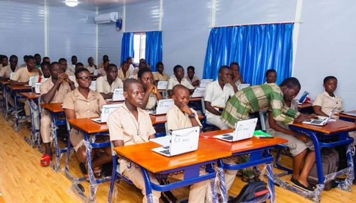 Des élèves en uniforme sont assis en rangée face à des ordinateurs portables dans une salle de classe éclairée et équipée
