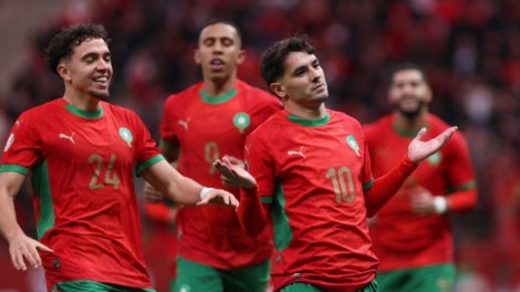 Quatre joueurs en maillot rouge et short vert célèbrent un but lors d’un match de football