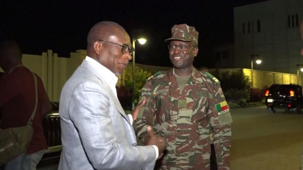 Un homme en costume clair serre la main d’un militaire en tenue de camouflage dans une rue de nuit
