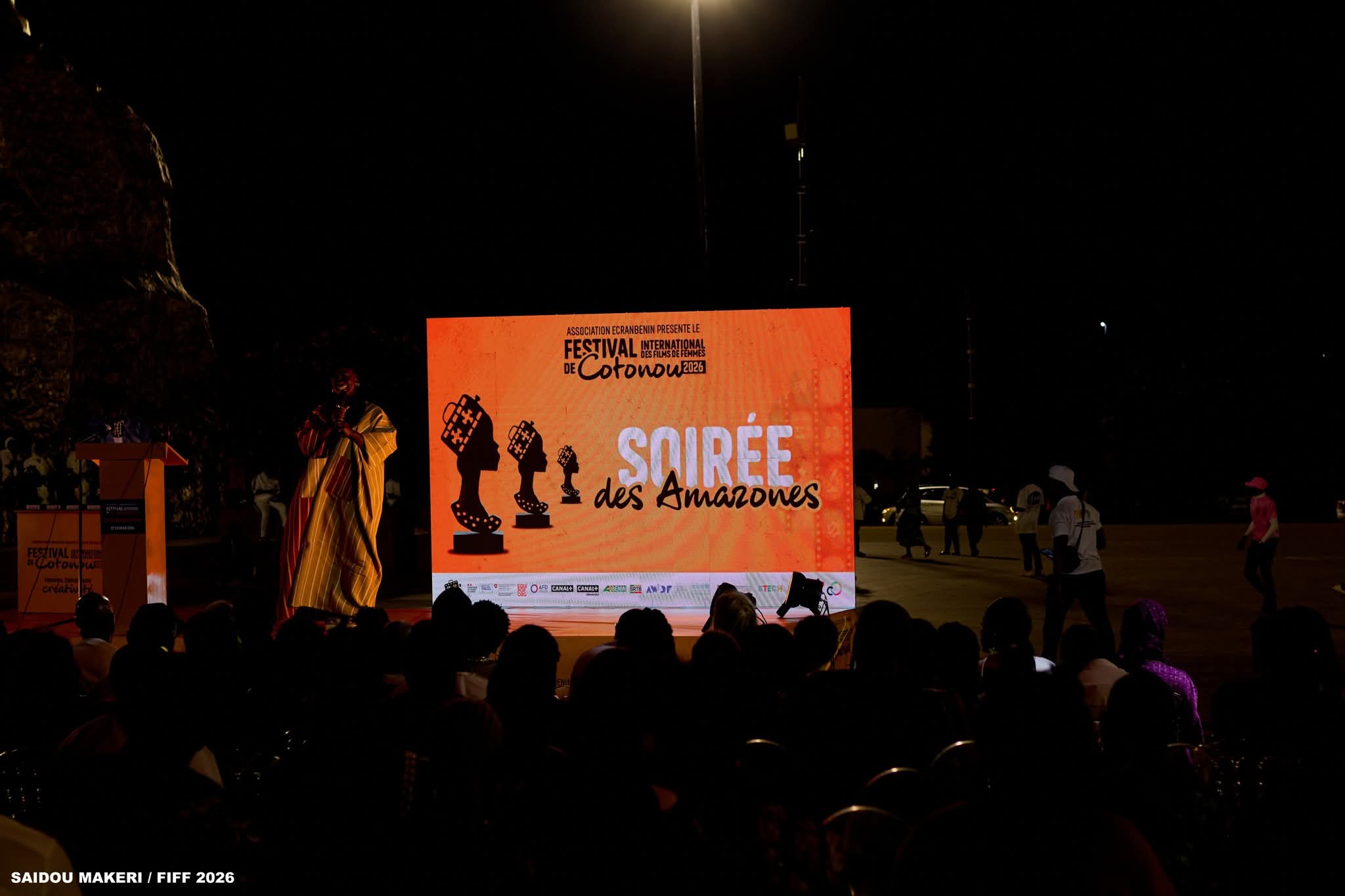 Une foule assise regarde un écran lumineux affichant « Soirée des Amazones » lors d’un événement nocturne en plein air