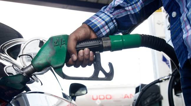 Main tenant une pompe verte remplissant un réservoir de voiture noire dans une station-service