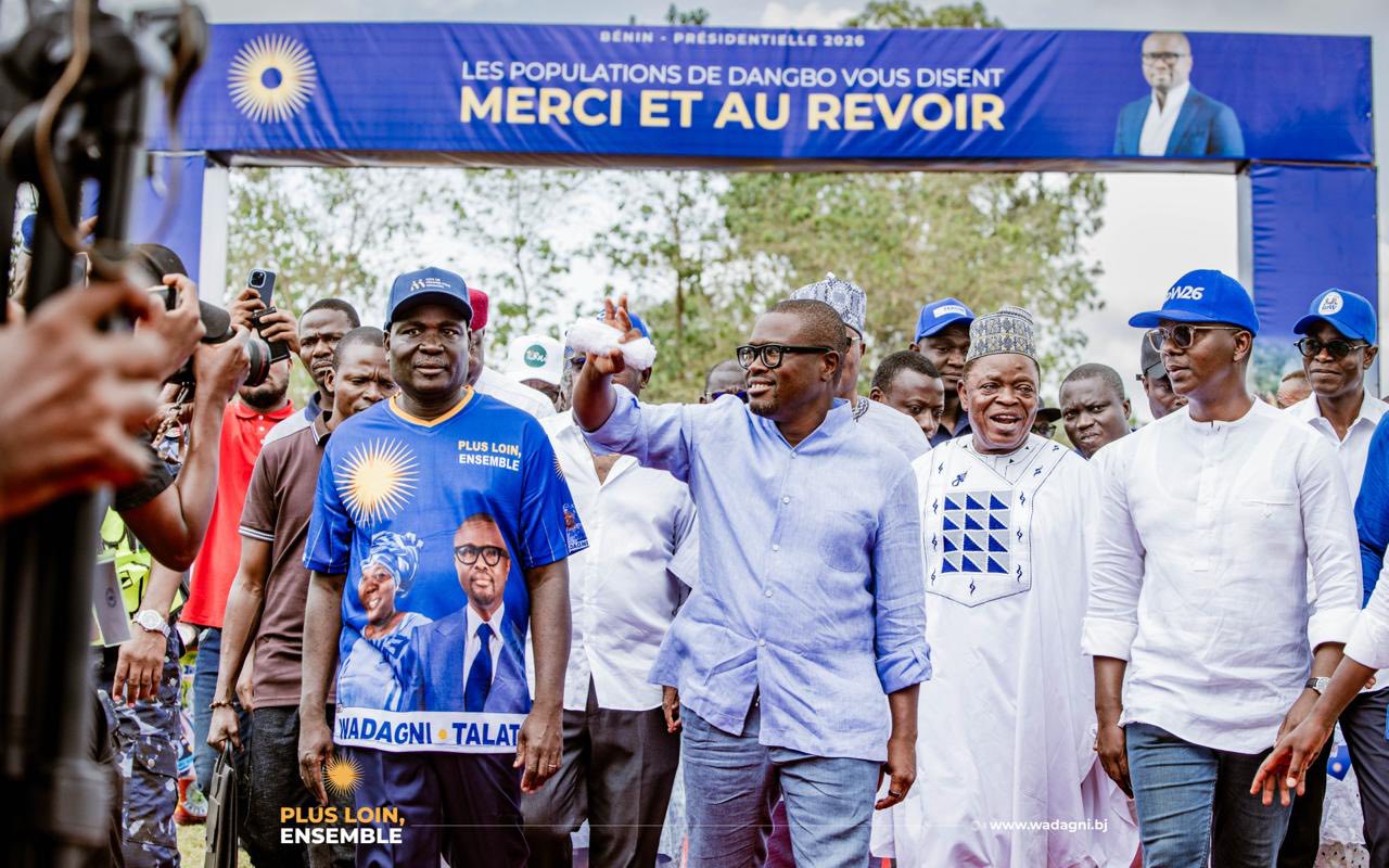 Un groupe d’hommes marche sous une banderole bleue où est écrit un message de remerciement et d’au revoir adressé aux populations de Dangbo