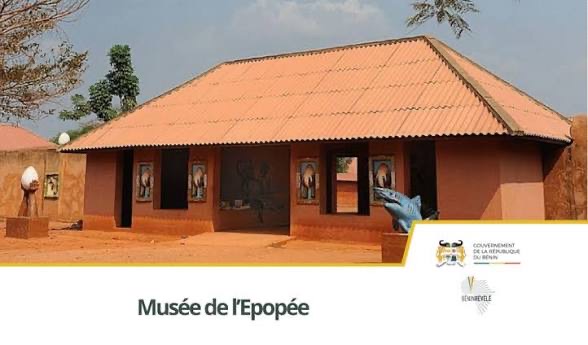 Bâtiment en terre cuite avec un toit en tôle et une fresque murale, entouré de végétation sous un ciel bleu