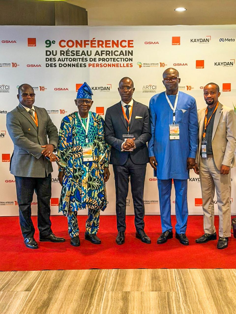 Cinq hommes debout sur un tapis rouge devant un panneau avec le titre de la conférence du Réseau Africain des Autorités de Protection des Données Personnelles