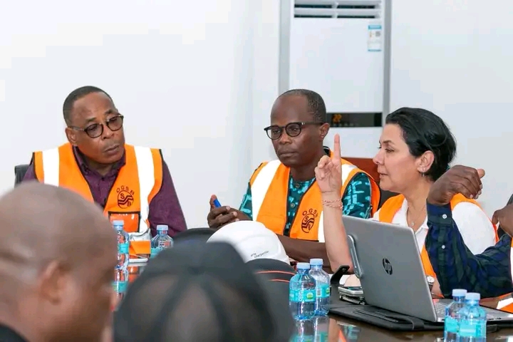 Personnes en gilets orange réunies autour d'une table avec des bouteilles d'eau, un casque blanc et un ordinateur portable.