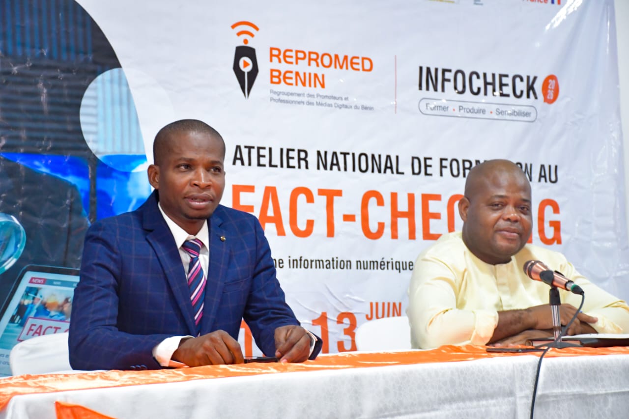 Deux hommes assis à une table lors d’un atelier sur le fact-checking avec une bannière en arrière-plan affichant les logos REPROMED BENIN et INFOCHECK