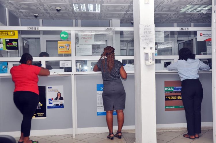 Trois femmes debout au guichet d’un établissement bancaire attendant leur tour de service