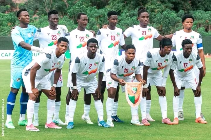 Onze joueurs de football posent en formation sur un terrain vert avec des maillots blancs ornés d'un drapeau multicolore