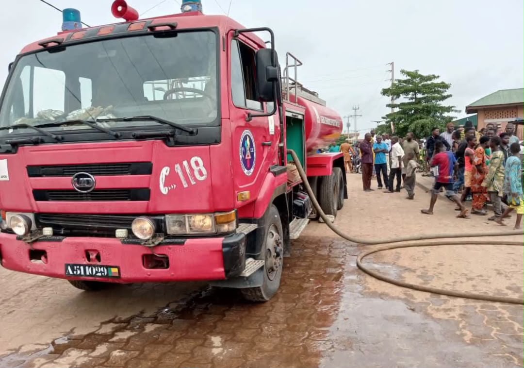 Camion de pompier rouge avec des habitants rassemblés sur une route pavée sous un ciel gris