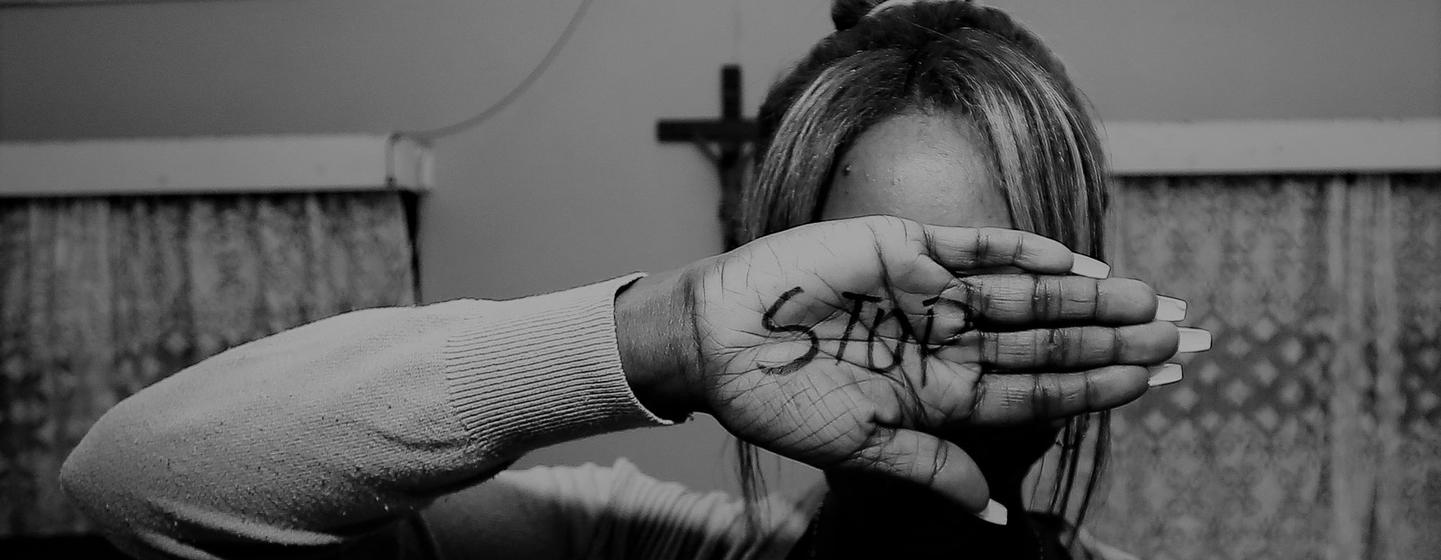 Une personne cache son visage avec une main où est écrit le mot « STOP » en lettres majuscules